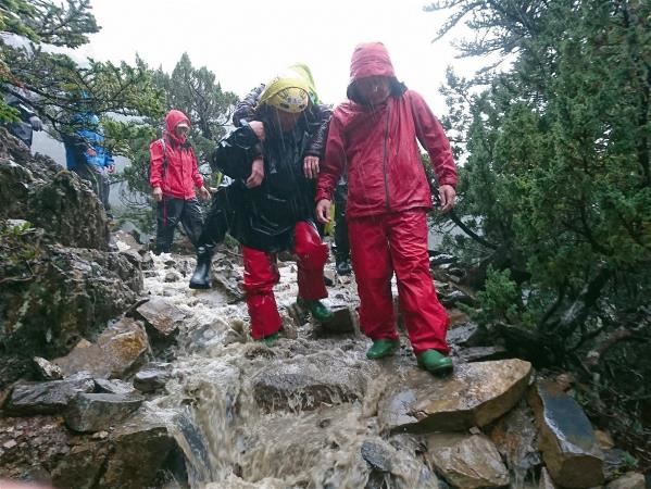 巡查員是救援的第一線。圖為2019年梅雨期間，頂著傾盆大雨和低寒氣溫，蕭玉山背著清晨攻頂拍照時遭雷擊的女山友，與前來馳援的消防隊員會合後，輪流將人背下山。（蕭玉山提供）