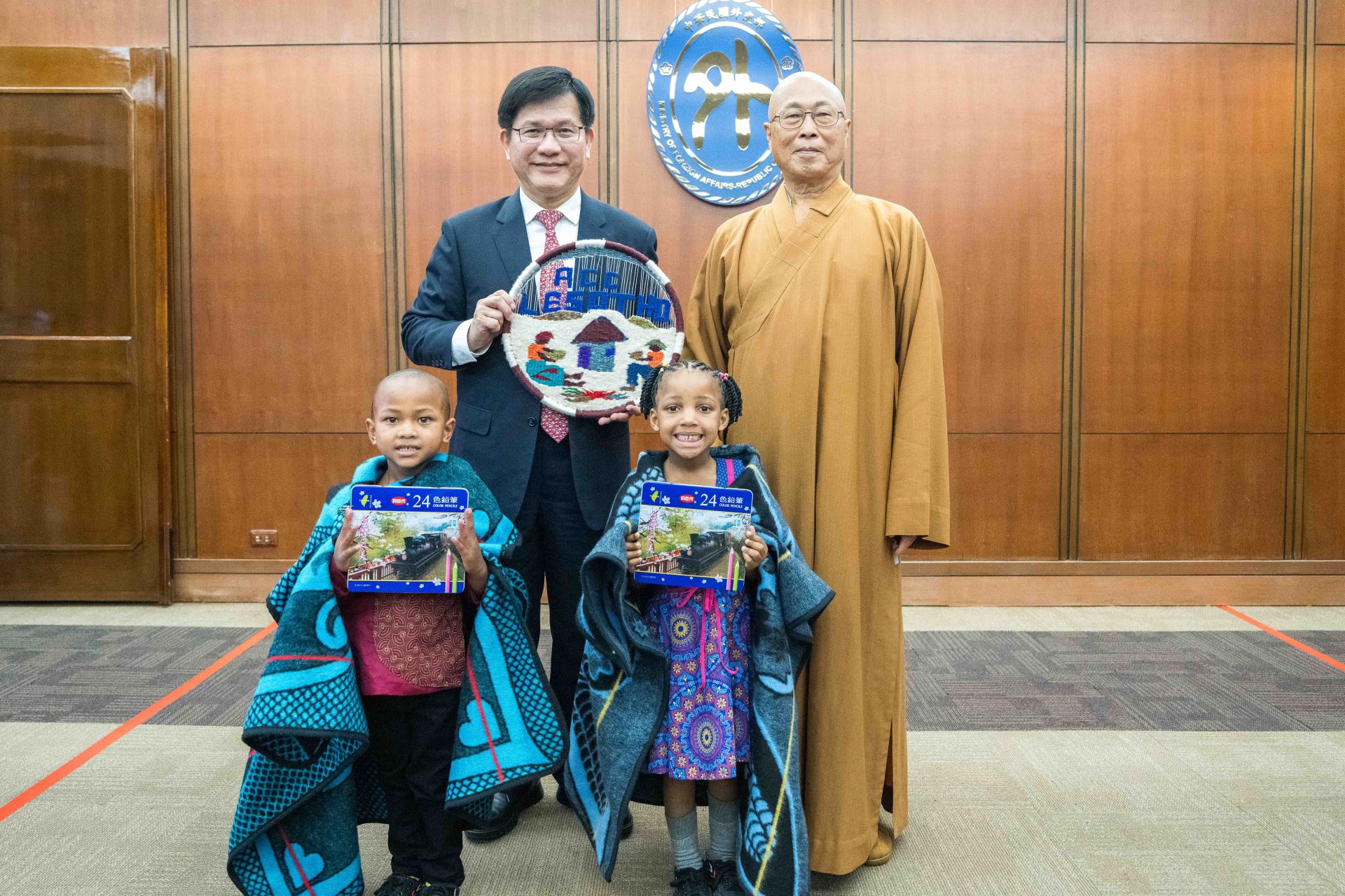阿彌陀佛關懷中心發起人慧禮法師（右後）及該中心院童代表致贈賴索托紀念品予外交部長林佳龍（左後）。