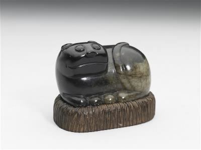 〈墨玉貓〉黝黑皮色是人工染色而成，在貓臀部可見原始的青白玉質。作品小巧，單手可握，應是把玩之作。