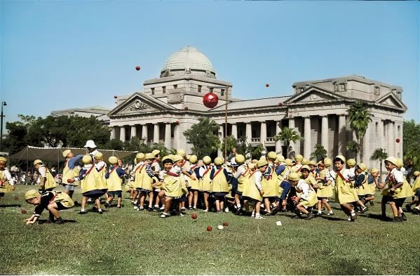 幼稚園的運動會,背景為今二二八和平紀念公園內的台灣博物館。王佐榮還考證出孩童玩的遊戲是源自西班牙語地區的「Piñata」,遊戲規則要用沙包把懸吊的紙糊彩球擊破;依據日本的習俗,分成的兩隊當然是以紅白兩色區分。(出自《彩繪鄧南光》
