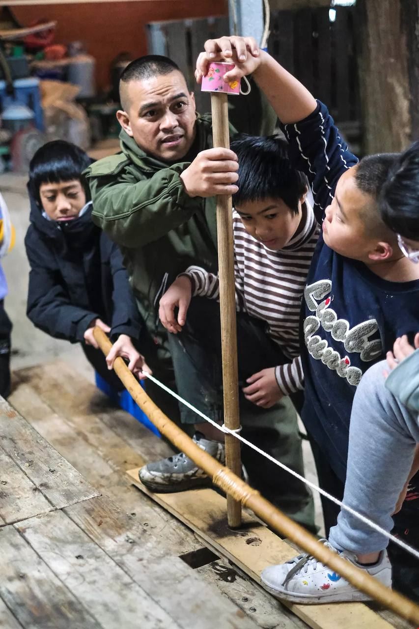 許勤指導孩子們用傳統弓鑽木取火，費力鑽磨了許久，才終於冒出一點火星，體驗以前生火的不容易。