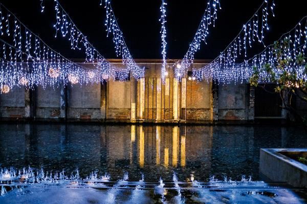 Hanging white lights and the illuminated poem “Summer Scenery” are reflected in the water of this pebble-filled pond, creating a magical beauty.